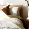 swath of sunlight shines across a well made bed and bedside table with a vase of cotton plants